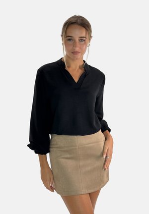 Blusa nera a maniche lunghe con scollatura a V e polsini arricciati, abbinata a una mini gonna in suede beige con una texture liscia e un design semplice.