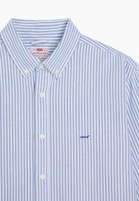 Chemise boutonnée à rayures bleues et blanches, dotée d'un col classique, de boutons blancs et d'un petit logo Levi's bleu sur la poitrine gauche.