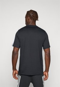 Zwarte t-shirt met korte mouwen en een ronde halslijn, voorzien van witte strepen aan de zijkanten en een gladde, katoenen textuur.