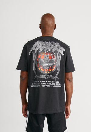 Czarny bawełniany t-shirt z dużą grafiką na plecach, przedstawiającą globus oraz nazwy miast w białym i czerwonym kolorze, utrzymaną w metalicznym stylu.
