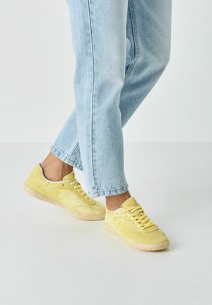 Gule mockasinsneakers med tekstureret finish, med snørelukning og gummisål. Kombineret med lyseblå cowboybukser.