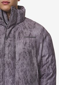 Gewatteerde jas van gestructureerde grijze stof met hoge kraag. Voorzien van een ritssluiting en een logo-accent aan de voorkant.