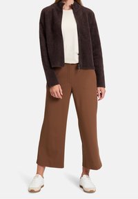 Faux fur jacket in dark brown with a high neckline, paired with brown wide-leg trousers and white sneakers with beige accents.
