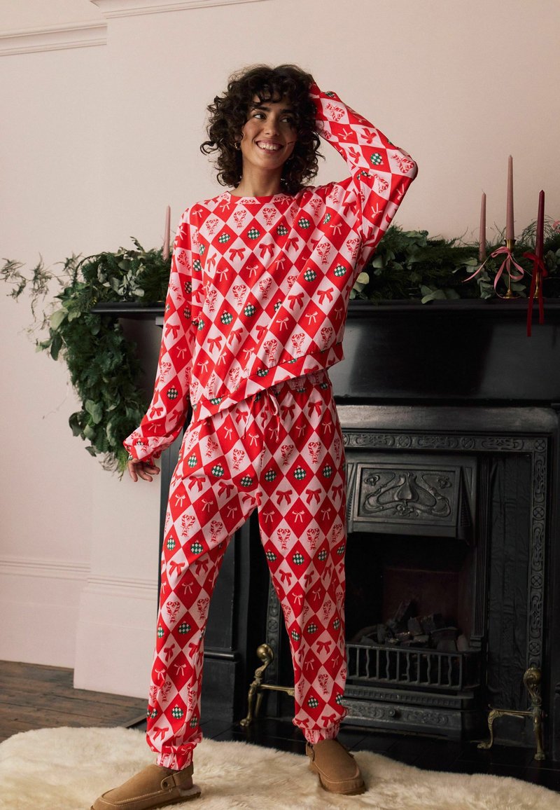 Ensemble de détente à motifs rouges avec un design en diamant et des accents verts et blancs. Le tissu semble doux et la coupe est décontractée avec des poignets élastiques.