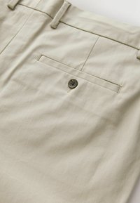 Pantaloni beige realizzati in tessuto testurizzato con una tasca posteriore dotata di un bottone scuro. Design aderente con vita standard e passanti per la cintura.