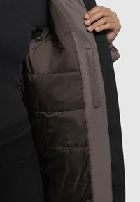 Schwarze Außenjacke mit einer grauen, gepolsterten Fütterung, die sichtbar ist. Die Fütterung hat eine glatte Textur und eine Innentasche.