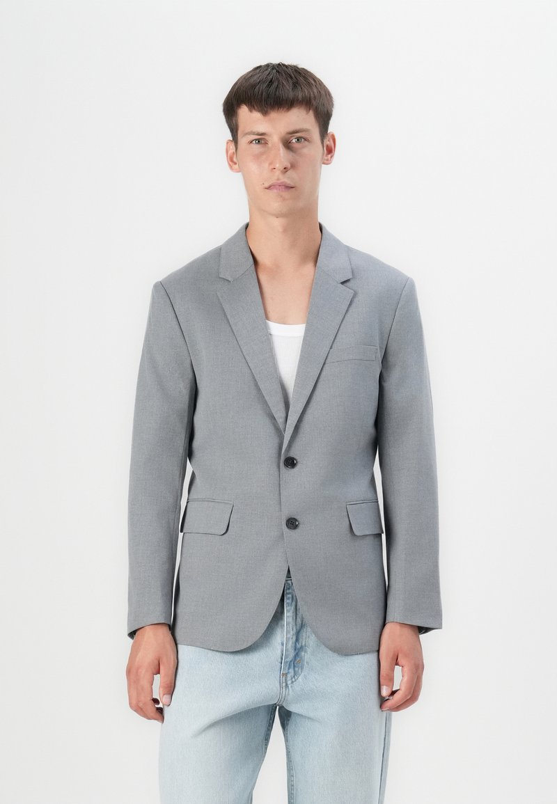 Gray blazer made of smooth fabric, featuring notch lapels, two front pockets, and two black buttons. Paired with light denim pants.