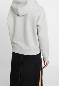 Sudadera gris con capucha, puños y dobladillo acanalados, combinada con una falda negra que presenta una abertura lateral y costuras en contraste.