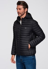 Chaqueta plumas negra con capucha, que cuenta con secciones acolchadas horizontales, cierre de cremallera completo y dos bolsillos laterales.