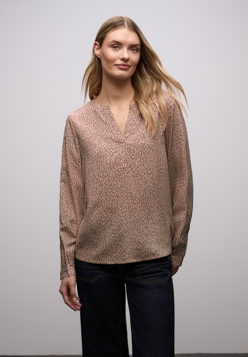 Blouse à manches longues en tissu doux, avec une base beige ornée d'un imprimé léopard marron et un col en V. Associée à un jean foncé.