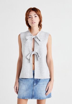 Gray sleeveless cardigan with a V-neck and two bow ties at the front, featuring a ribbed texture. Paired with a blue denim mini skirt.
