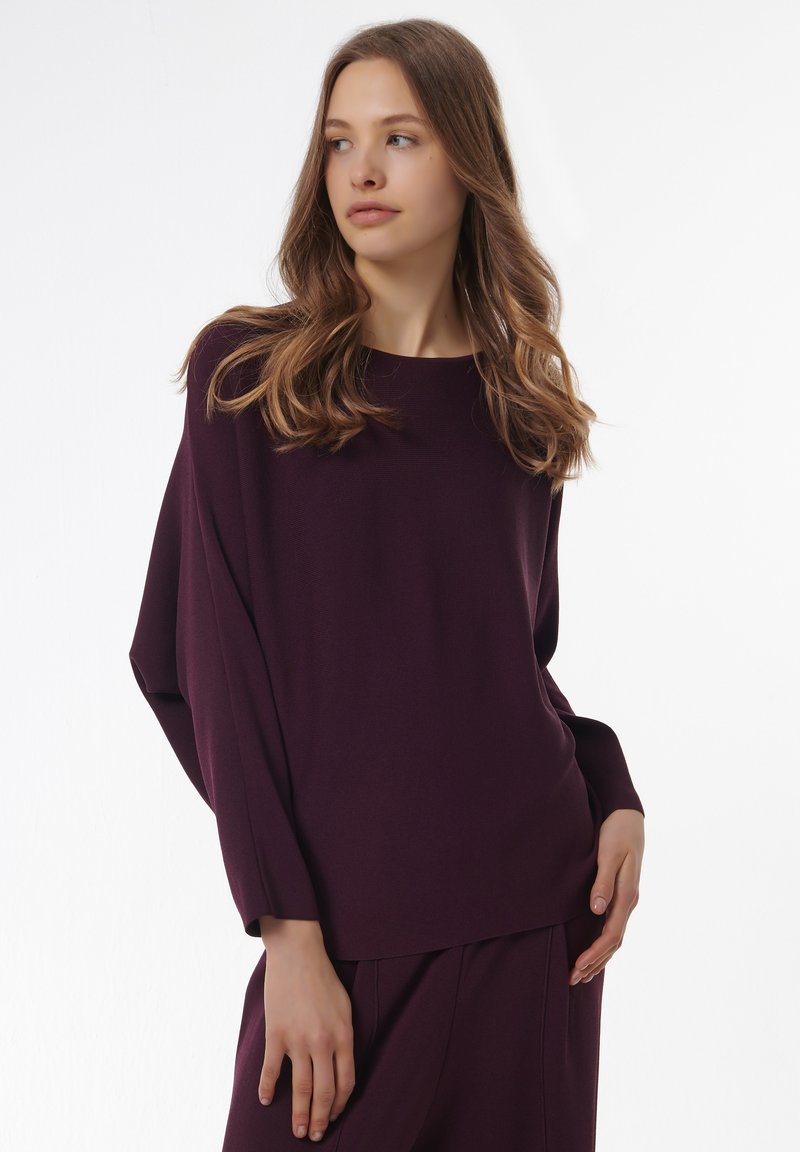 Pull violet surdimensionné avec une encolure large et des épaules tombantes, fabriqué en tissu doux, avec une texture côtelée et des manches longues.
