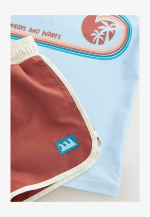 Heledsinine lühikeste varrukatega särk logoga, mis on kombineeritud roostes värvi lühikeste pükste ning valge äärepikkuse ja sinise laine logoplaadiga.