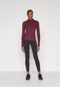 Bordāna sporta krekls ar rāvējslēdzēju un garām piedurknēm, kombinēts ar melnām legingām un melniem sporta apaviem. Gluda auduma un pieguļošs dizains.