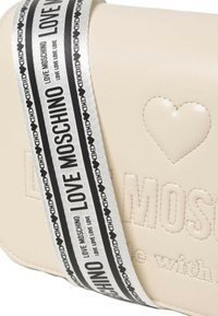 Borsa color crema con cuore in rilievo e logo "LOVE MOSCHINO". Presenta una tracolla bianca e nera con testo ripetuto e dettagli a forma di cuore.