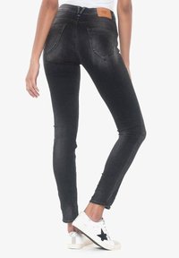 Czarne obcisłe jeansy wykonane z denimu, z wysokim stanem, dwoma tylnymi kieszeniami oraz beżową skórzaną naszywką z tyłu w pasie. Białe trampki z czarną gwiazdą.