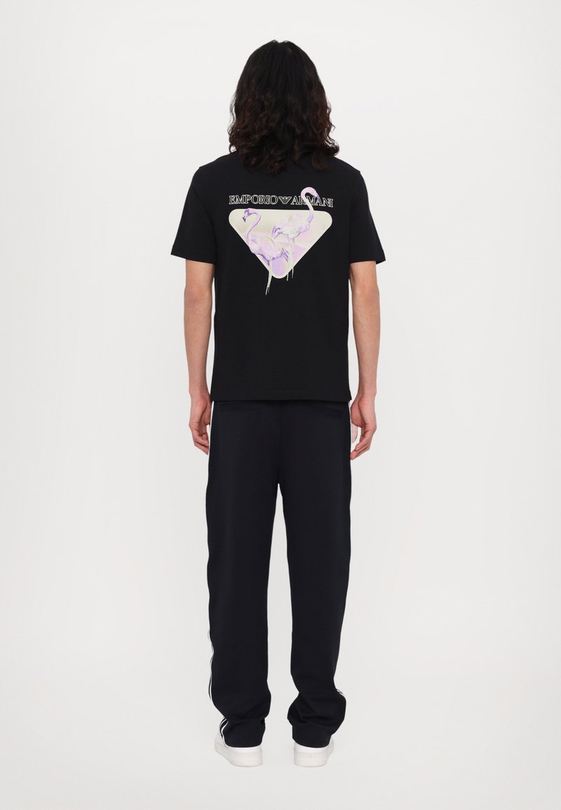 Black t-shirt with a triangle graphic on the back featuring pink and purple flamingos. Soft fabric, relaxed fit. Paired with dark pants.