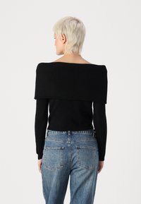 Schwarzer gerippter Off-Shoulder-Pullover mit langen Ärmeln, kombiniert mit hoch taillierten hellblauen Jeans mit Gesäßtaschen.