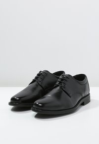 Black leather dress shoes with a smooth finish, rounded toe, and narrow laces. Features a low heel and stitched detailing along the sides.