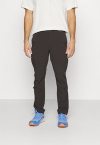 Črne lahke hlače s slim fit krojem, z zadrgo in gladko teksturo. V kombinaciji z modrimi športnimi čevlji z oranžnimi detajli.