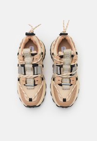 Baskets en maille et caoutchouc beige avec des accents noirs, dotées de plusieurs sangles, d'une semelle texturée et de détails de marque sur la languette.