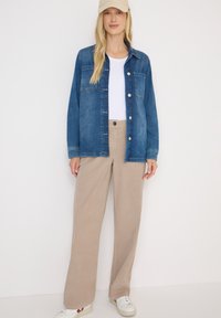 Granatowa kurtka dżinsowa z guzikami i kieszenią na piersi, zestawiona z beżowymi spodniami o szerokich nogawkach. Biała koszulka pod spodniami i beżowa czapka. Białe sneakersy.