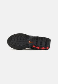 Nike-kenkäpohja mustasta kumista punaisilla korostuksilla. Ominaisuuksiin kuuluu teksturoitu pito, jossa on pyöreitä ja suorakulmaisia kuvioita sekä oranssi logo.