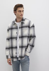 Black and white plaid shirt made of soft fabric, featuring large checked patterns, button closure, and a relaxed fit. Worn over a white t-shirt.