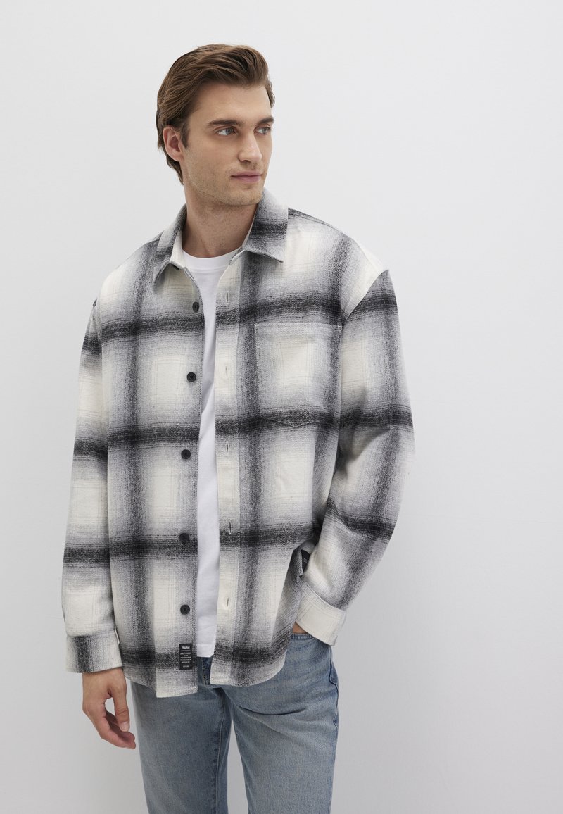 Black and white plaid shirt made of soft fabric, featuring large checked patterns, button closure, and a relaxed fit. Worn over a white t-shirt.