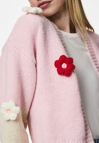 Ροζ πλεκτό κασκόλ με μπαλόνι μανίκια, που διαθέτει λευκά και κόκκινα κεντημένα λουλούδια στους ώμους. Μαλακή υφή και ανοιχτό σχέδιο.