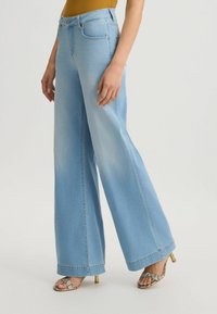 Jeans larghi di denim di color blu chiaro, con vita alta, sfumature sottili e un classico design a cinque tasche. Abbinati a sandali con tacco.