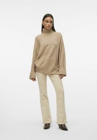 Beige coltrui met een relaxte pasvorm, lange mouwen en zijsplitten, gecombineerd met lichtgekleurde flared broeken en bruine haklaarzen.