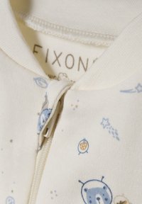 Krämfärgad zip-up bodysuit med ett mönster av blå björnar, stjärnor och cirkulära mönster. Mjuk tyg med ribbad textur nära kragen.