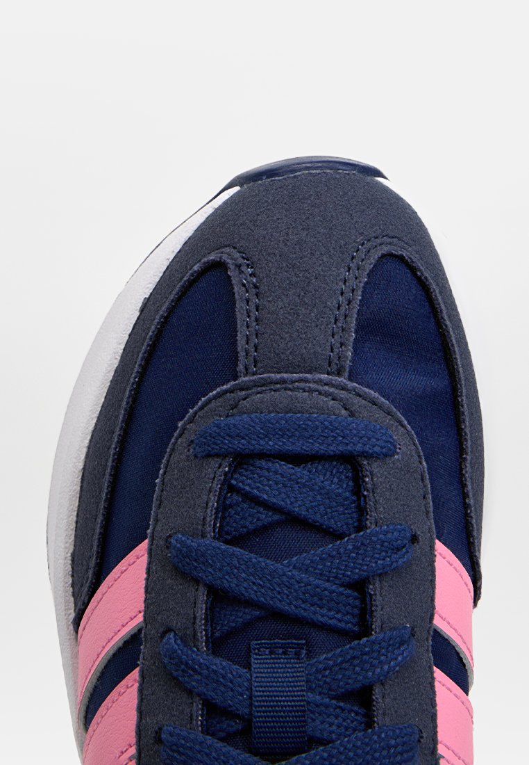 Chaussures de sport bleu marine avec un dessus en daim et en tissu, rayures roses, lacets ronds et semelle en caoutchouc blanche. Accents en tissu texturé présents.