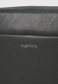 Sac en cuir noir avec une texture lisse et un logo "Valentino" en argent. Forme rectangulaire avec un design minimaliste.