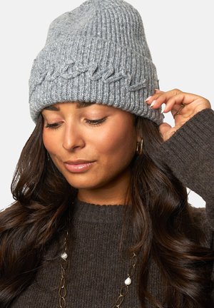 Grijze gebreide beanie met een gewatteerd kabelpatroon, dikke ribbels en een zachte uitstraling. Laag gedragen en gedeeltelijk omgevouwen aan de rand.