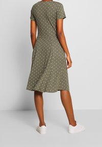 Sukienka w oliwkowe kropki z krótkimi rękawami, dopasowanym gorsetem i rozkloszowanym dołem. Wykonana z miękkiego materiału, zestawiona z białymi trampkami.
