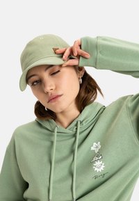 Light green cotton hoodie with a kangaroo pocket, drawstrings, floral graphic accents, paired with a matching cap featuring a logo patch.