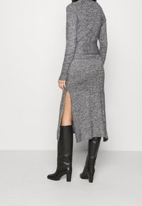 Abito a maglia grigio con maniche lunghe, vita aderente e spacco laterale. Abbinato a stivali neri fino al ginocchio, con texture liscia e design casual.