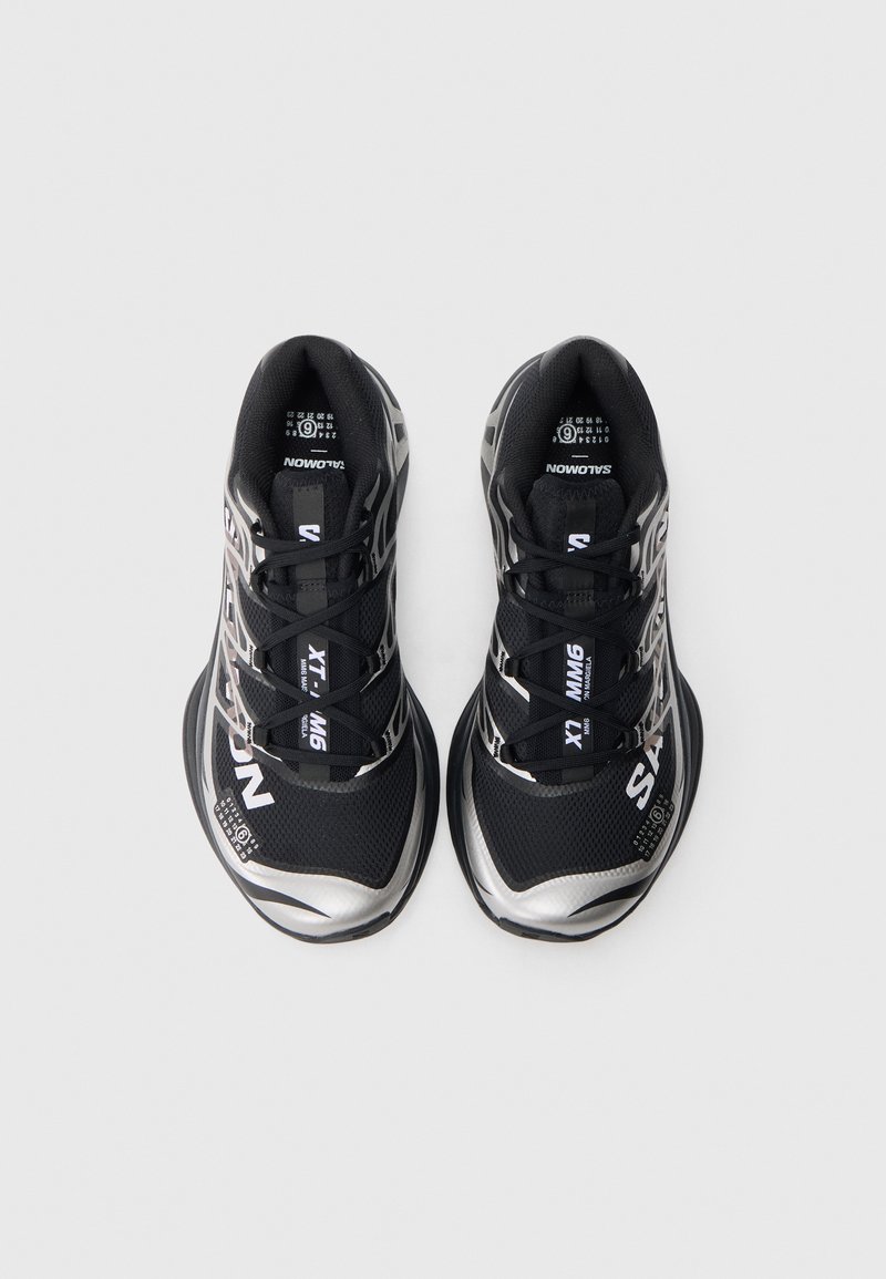 Black athletic shoes with a mesh upper, featuring silver accents, a textured sole, and logo detailing. Laces are threaded through reinforced eyelets.