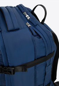 Modrý batoh vyrobený z odolné tkaniny s několika zipovými komorami, polstrovanými popruhy a nastavitelným černým sponovým popruhem.