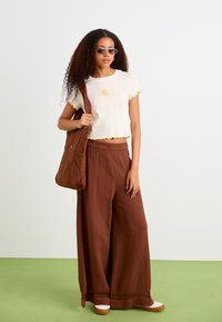 Pantaloni a gamba larga marroni, top corto color crema con ricami gialli e borsa trapuntata marrone. Texture liscia con un motivo sottile.