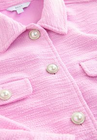 Pink textured jacket with pearl-like buttons and flap pockets, featuring a folded collar and a "NEXT" brand label inside the neckline.