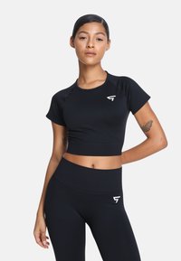 Czarny sportowy crop top oraz legginsy z wysokim stanem, wykonane z elastycznego materiału, z białym logo na górze i legginsach.
