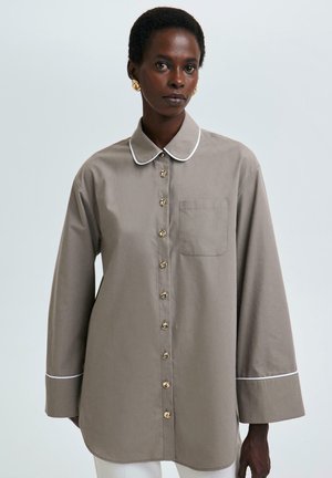 Hellbraune Button-Up-Bluse mit langen Ärmeln, weißen Paspeln an Kragen und Manschetten, ausgestattet mit einer Brusttasche und goldenen Knöpfen.