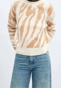 Suéter de punto a rayas tigre en beige y crema con cuello redondo y ribete acanalado; combinado con unos pantalones vaqueros de tiro alto en azul claro.