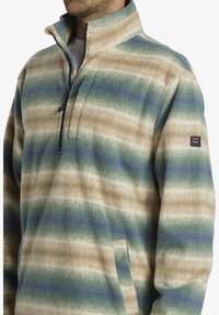 Pull en polaire avec un design à demi-fermeture éclair, motif rayé en crèmes, vert et bleu, avec un tissu texturé et des poches latérales.