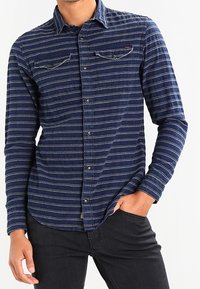 Camicia button-up blu navy con righe orizzontali bianche, due tasche sul petto e colletto. Il tessuto sembra strutturato con una leggera elasticità.