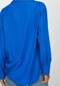 Camicia blu con bottoni, maniche lunghe, texture liscia e orlo curvo. Presenta un colletto classico e polsini con bottoni.