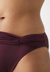 Burgundy high-waisted bikini bottom featuring a knotted detail at the waistband, smooth texture, and minimal stitching.